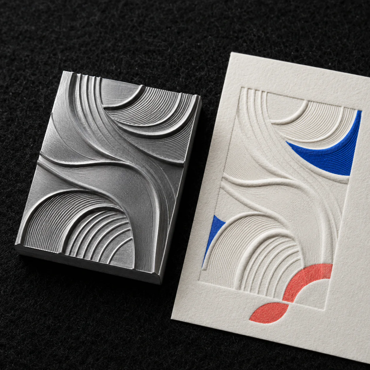 Steel embossing die beside the debossed cotton card it produces, on dark felt